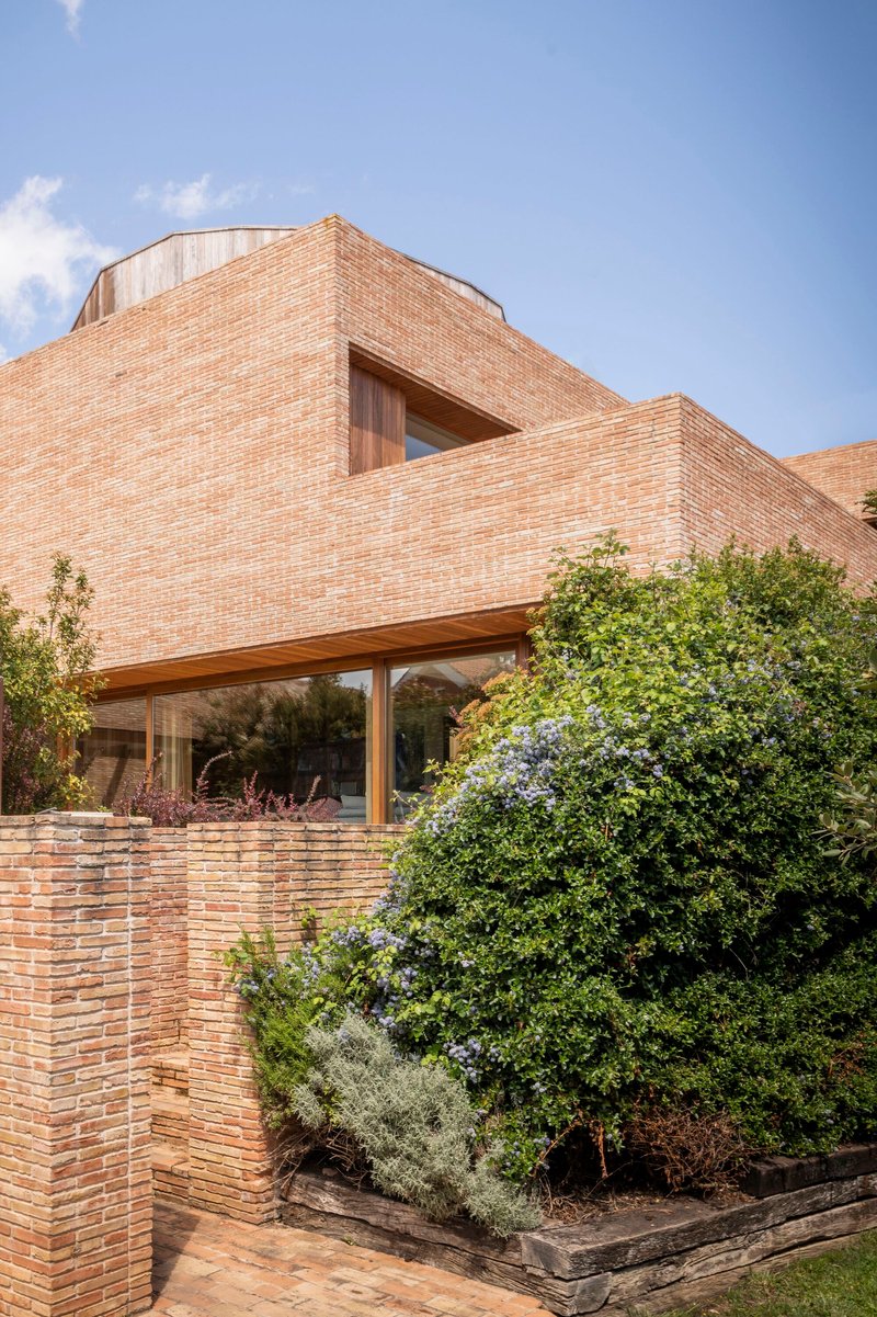 Cantilevered brick facade above a glazed living space with planted beds below