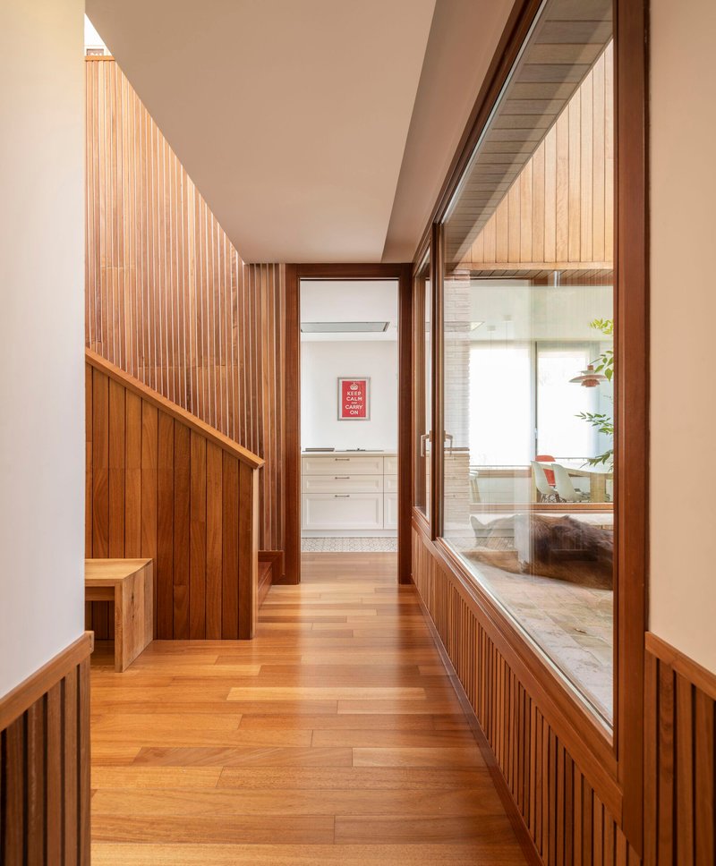 Timber-lined corridor with slat paneling leading to a kitchen beyond