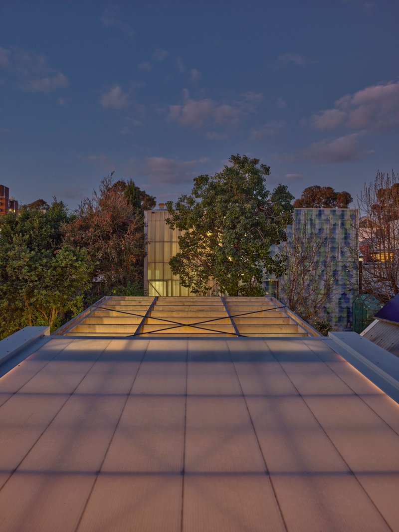Rooftop terrace with tiled paving and glass skylight panels overlooking neighboring treetops at twilight