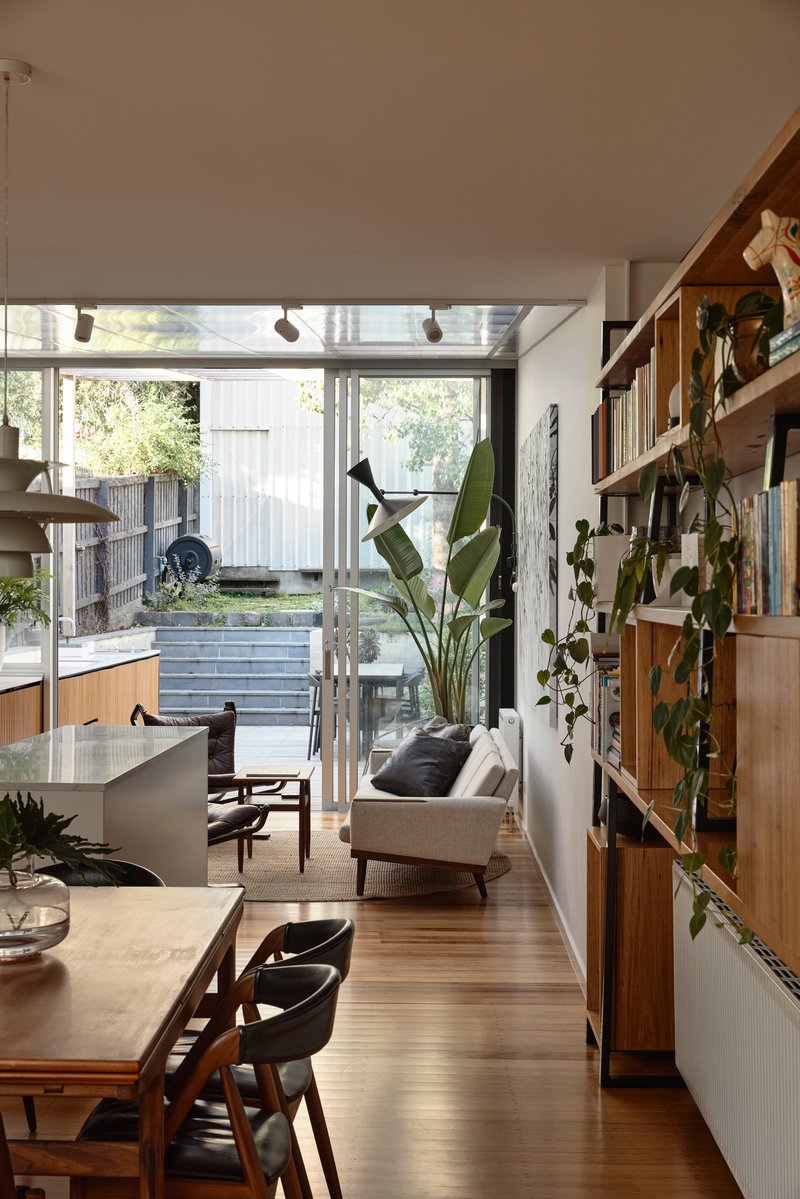 Corridor with timber shelving wall and glazed doors opening to sunlit courtyard and tree