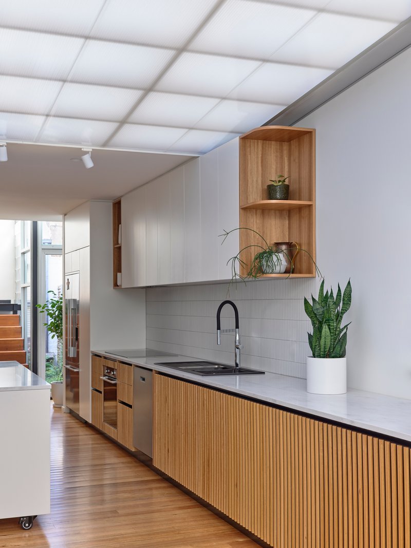 Galley kitchen featuring timber-slat cabinetry and open timber shelving with potted plants