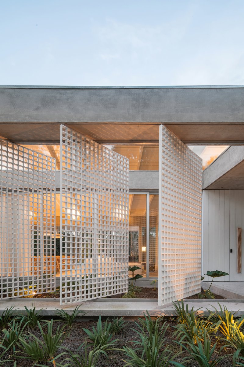 Perforated lattice screen panels illuminated from within at dusk with planted beds in foreground