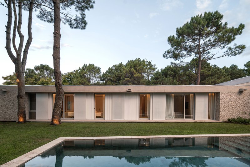 Pool terrace view of the linear facade with glazed openings and interior lights at dusk