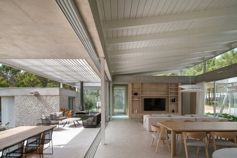 Living and dining area with exposed concrete beams and floor-to-ceiling glass opening to covered terrace