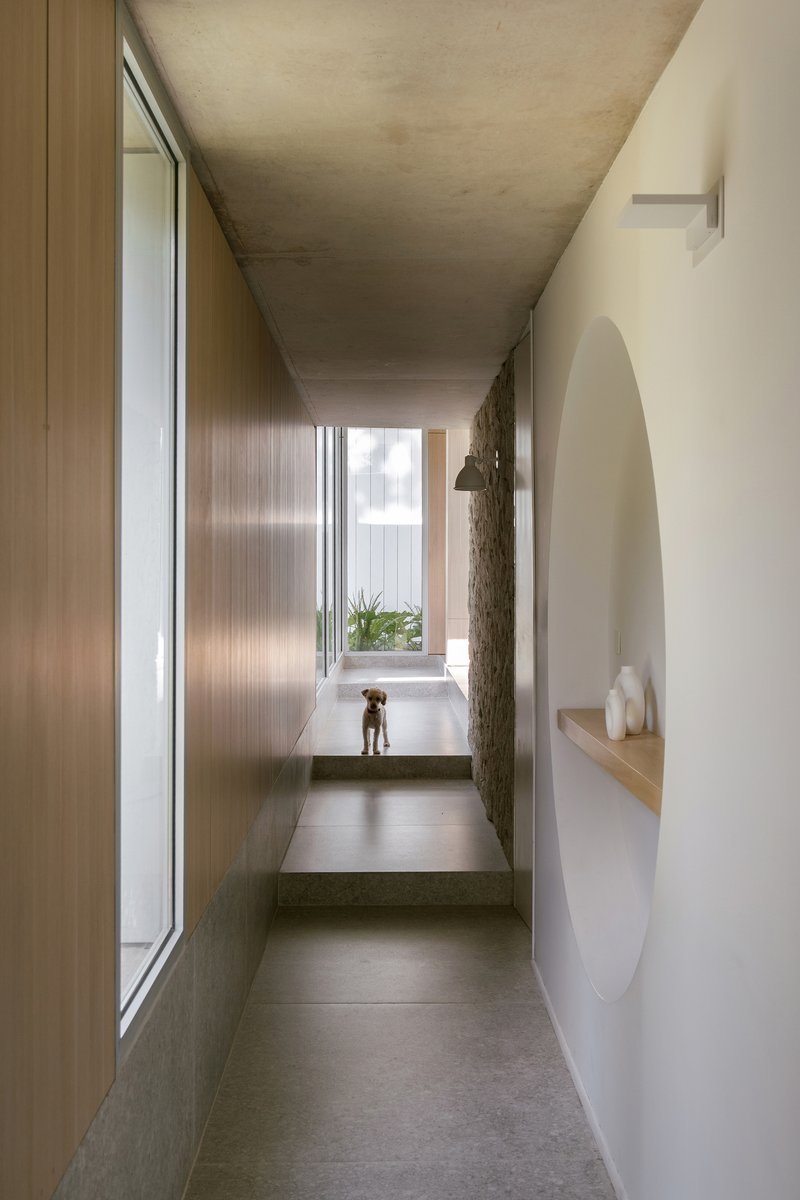 Narrow corridor with concrete ceiling, timber wall panels and arched niche with floating timber shelf