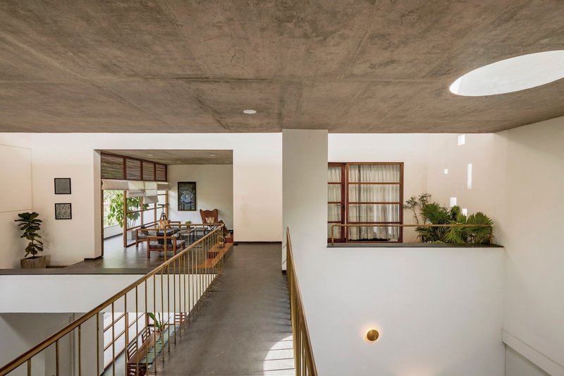 Upper-level corridor with exposed concrete ceiling, brass railings and potted plants in a window niche