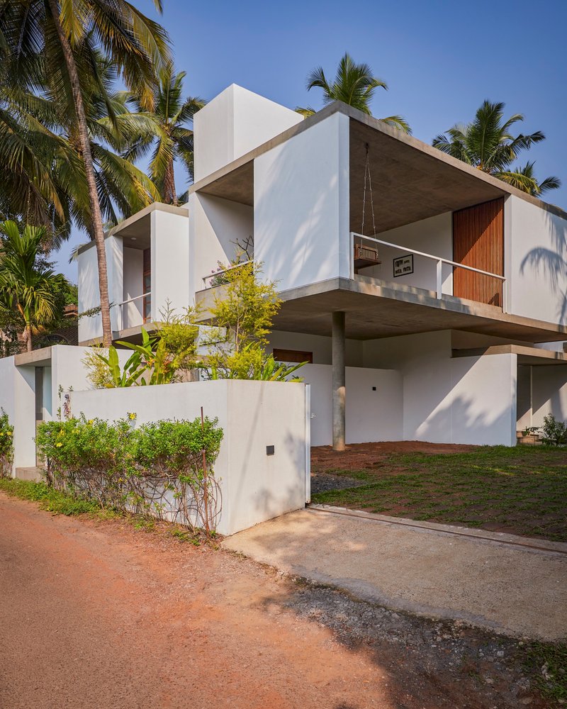 Street view of white cantilevered volumes with timber cladding among coconut palms under blue sky