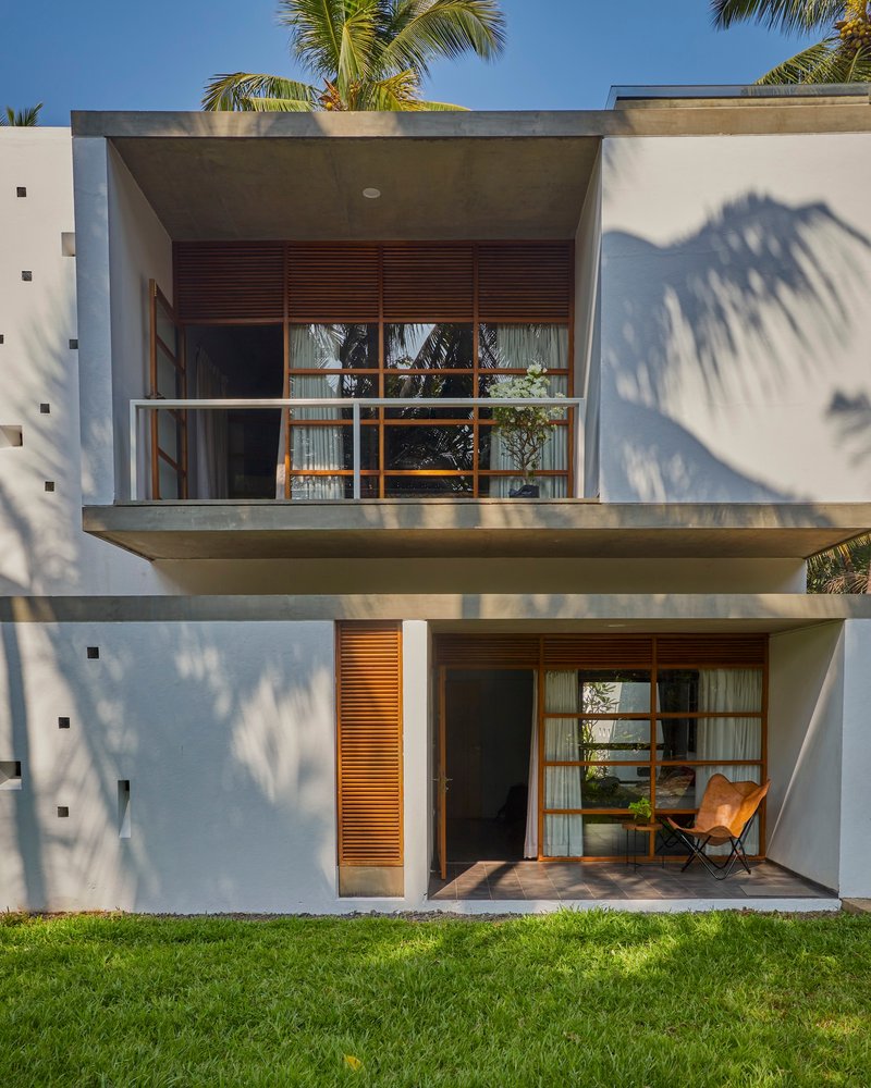 Two-story facade with cantilevered balconies and timber louvered panels framed by palm shadows