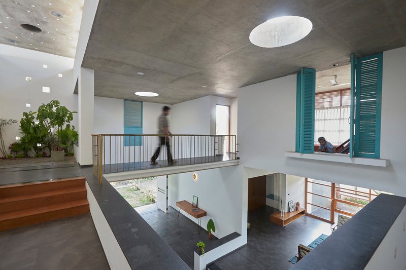Double-height interior space with brass railings, exposed concrete ceiling and a figure crossing the upper floor