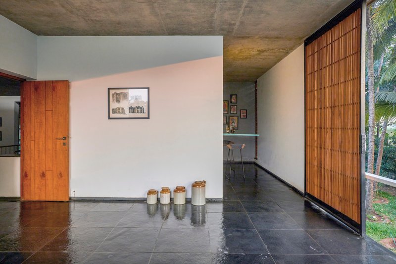 Hallway with black stone floor and sliding bamboo screen beside a timber door and concrete soffit