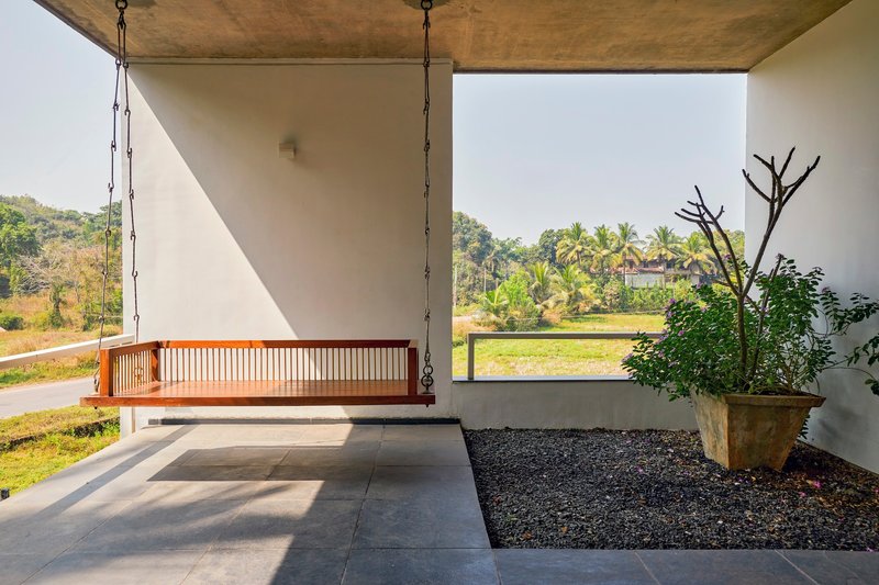 Covered porch with suspended timber daybed overlooking planted beds and distant palms