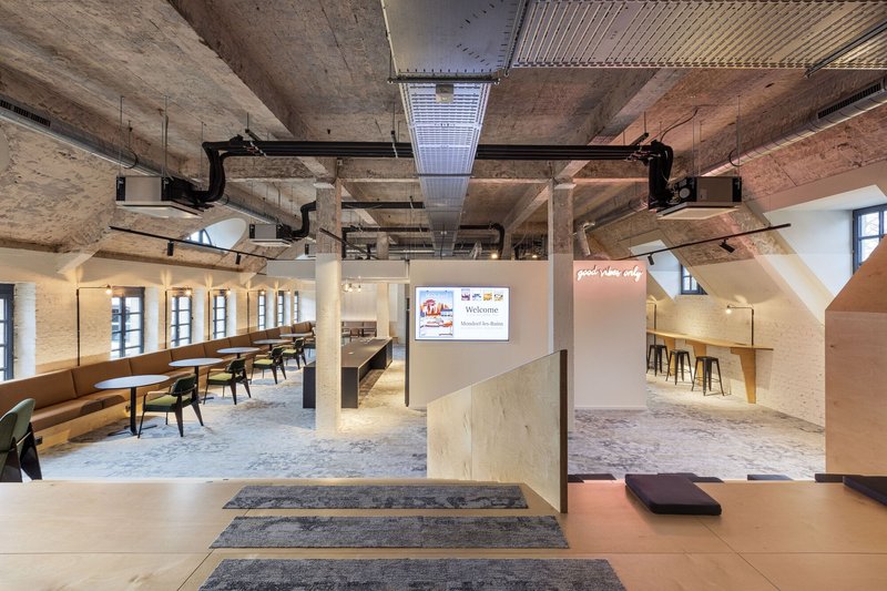 Open office interior with exposed concrete ceiling beams and wood-framed glass partitions under warm lighting