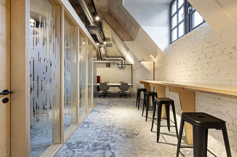 Corridor with timber counter and bar stools against whitewashed brick wall beneath sloped concrete ceiling