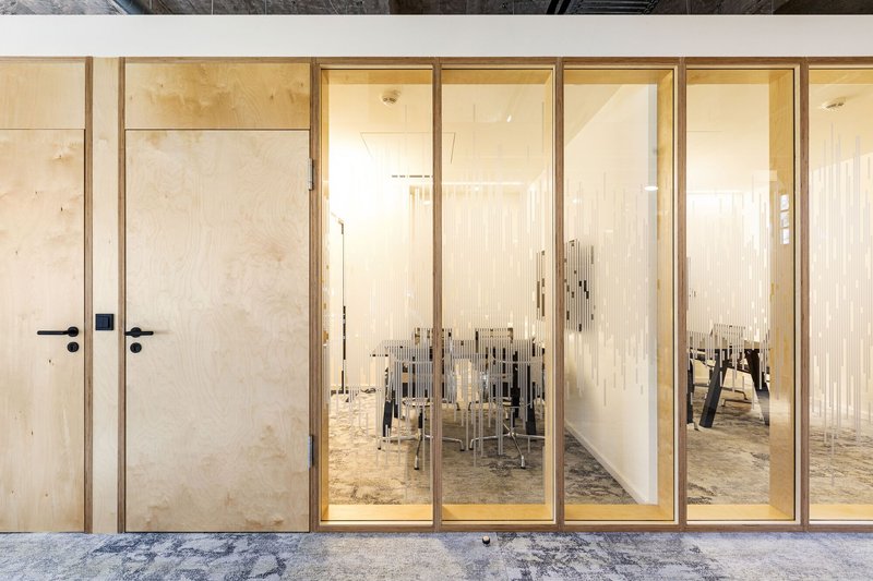 Corridor view through glazed timber screens revealing a meeting room with polished concrete floor