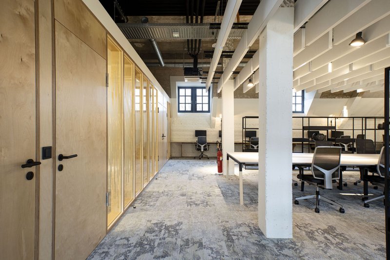 Office hallway lined with plywood sliding doors beneath exposed mechanical ducts and white columns