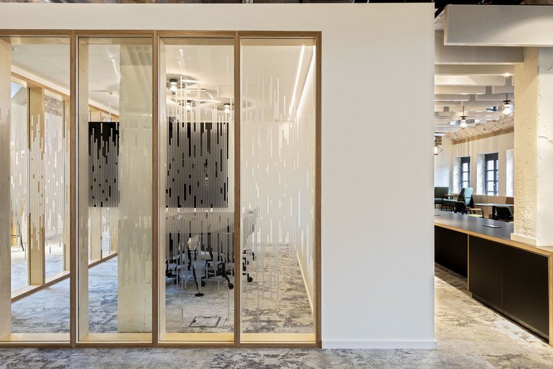 Glass partition wall with timber frame dividing the open office space under natural daylight