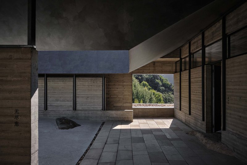 Interior courtyard with rammed earth walls, dark paving and a single boulder under filtered daylight