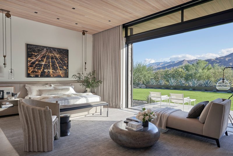 Bedroom with floor-to-ceiling glass doors opening to lawn and desert plantings beyond