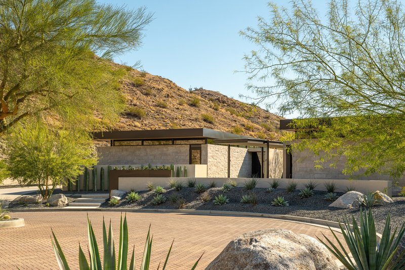 Front facade with stone walls and flat roofs amid desert planting and rocky hillside