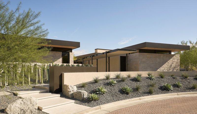 Entry approach showing stucco and stone volumes with cantilevered roofs in desert setting