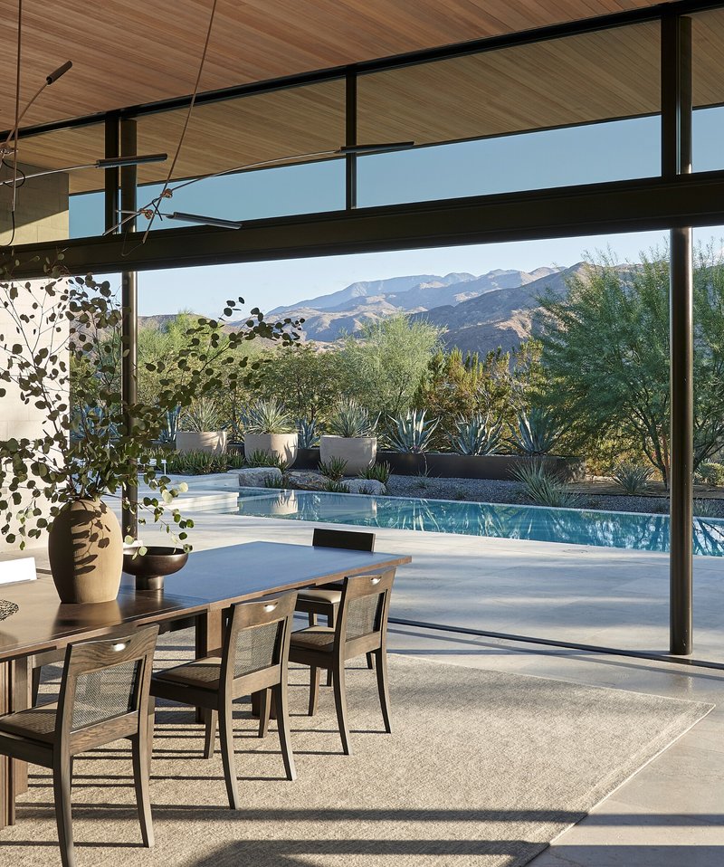Dining area with timber ceiling looking through glass walls to pool and desert landscape with mountains