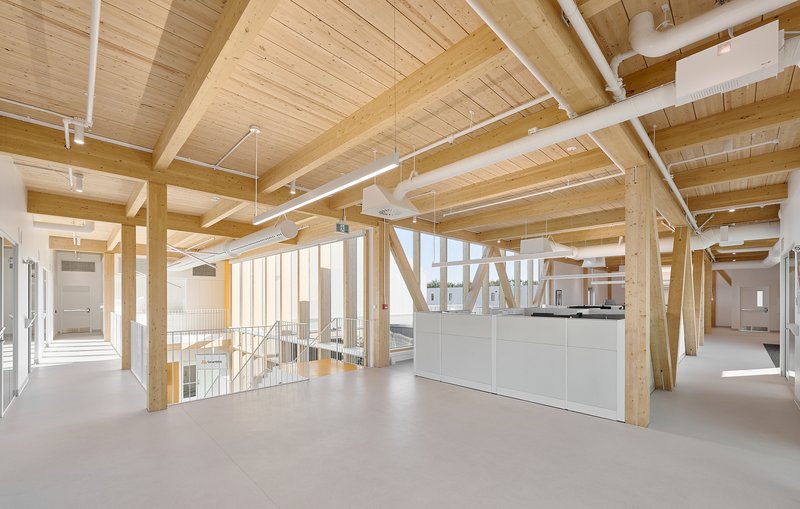 Upper-level open workspace with exposed timber beams and a white central millwork unit overlooking the floor below