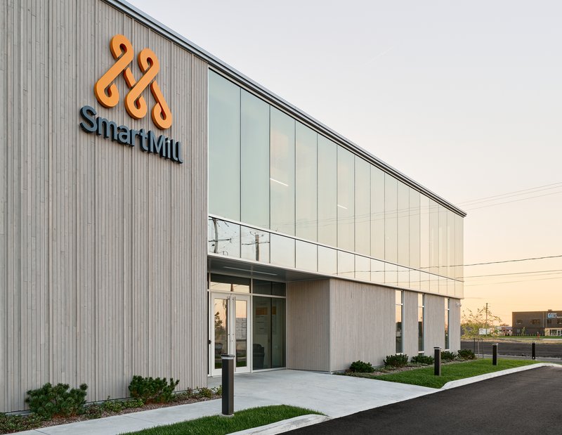 Entrance facade with vertical metal cladding and translucent panel upper story photographed at sunset