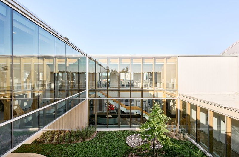 Interior courtyard with planted beds and sloped glass wall revealing office spaces beyond