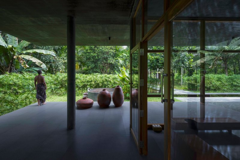 Open pavilion with polished floor and ceramic vessels looking toward garden with person standing outside