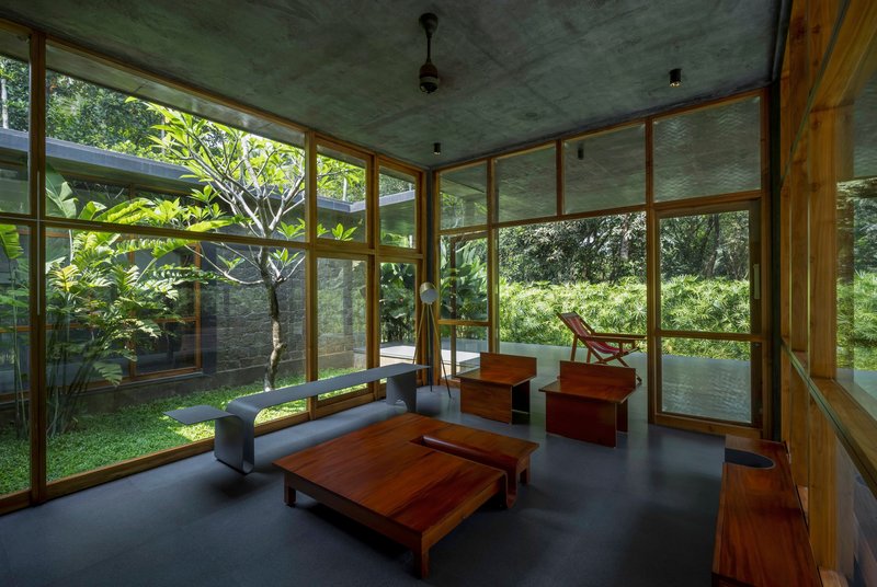 Timber-framed glazed living room with concrete ceiling and courtyard views under dappled light