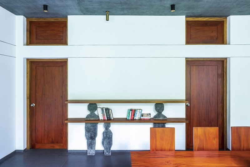 Double-height interior wall with symmetrical timber doors and suspended bookshelves flanked by two sculptures