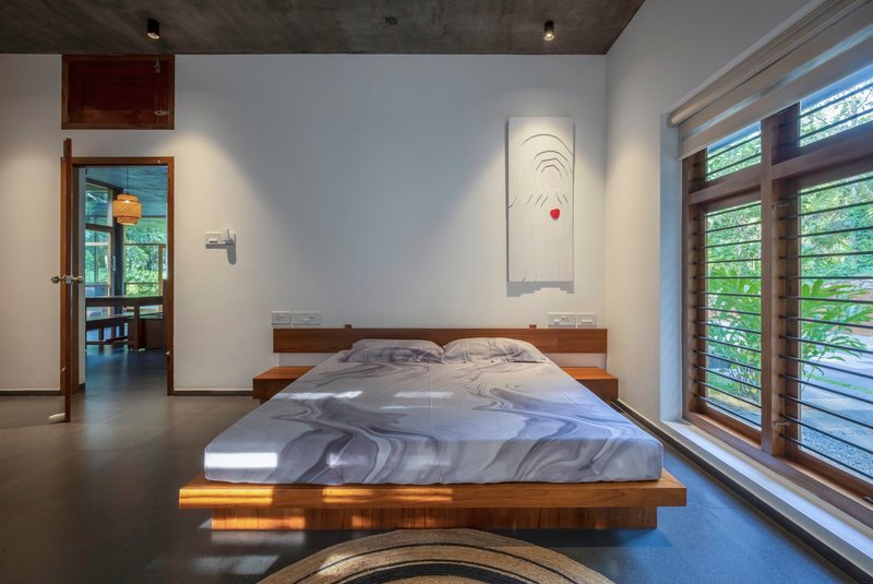 Bedroom with platform bed and horizontal louvered windows casting striped sunlight across the floor