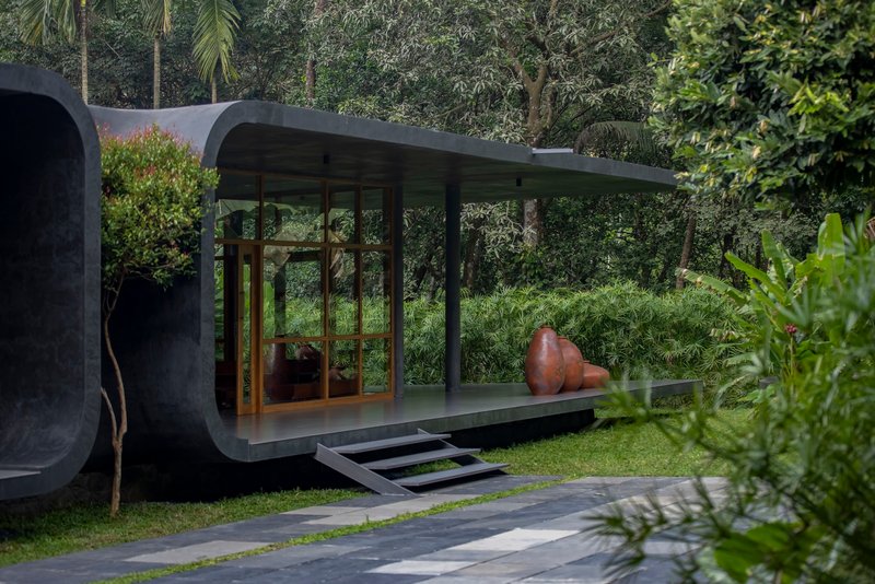 Glass pavilion with timber framing and curved concrete roof edge set in a lawn with tropical vegetation