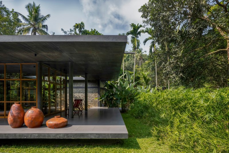 Covered terrace with concrete slab floor displaying three ceramic vessels alongside banana plants and palms