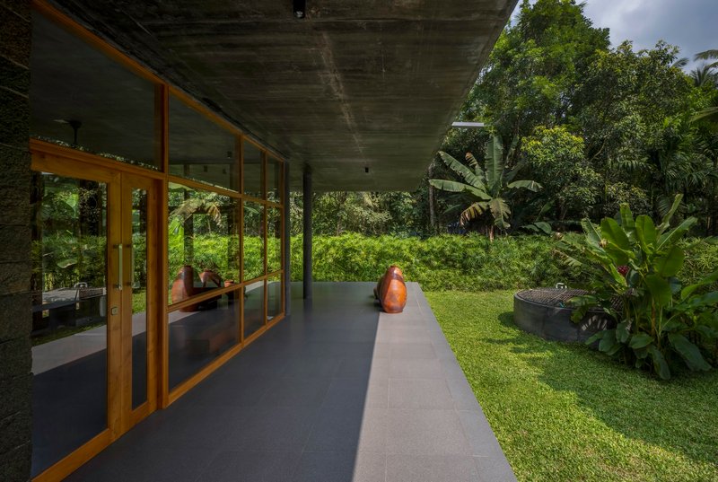 Concrete overhang sheltering a walkway with timber framed glazing overlooking a lawn and banana plants
