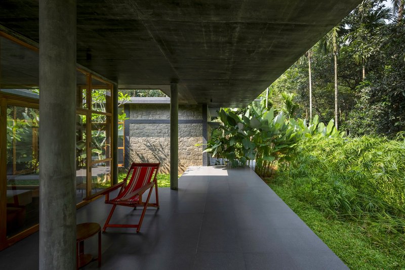 Covered passage with concrete columns and a red deck chair facing a stone wall and palms