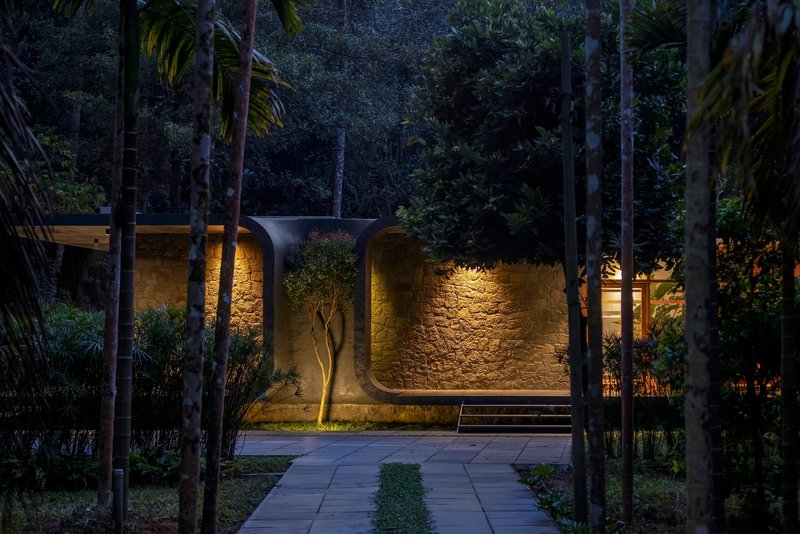 Night view of the illuminated stone facade with arched niches framed by palms and planted approach