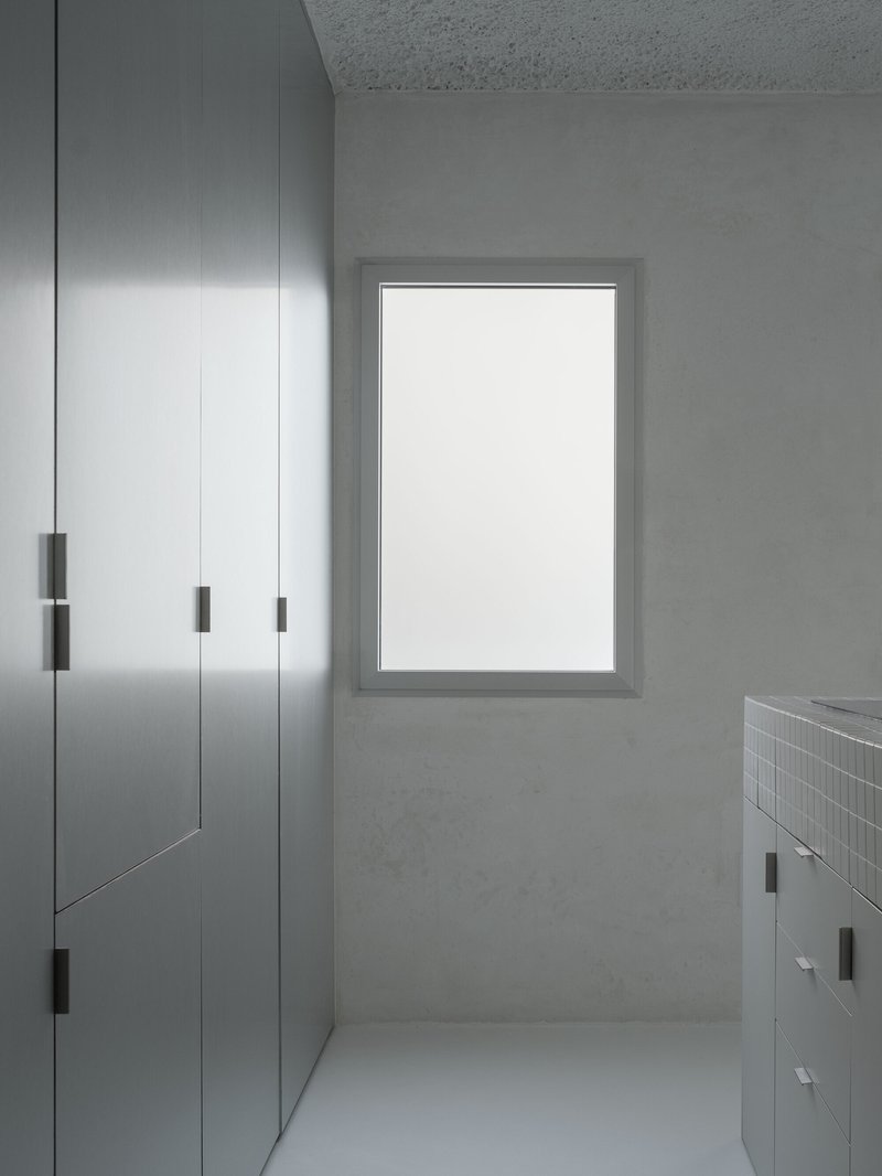 Corridor with brushed steel wardrobes, white-framed window and mosaic tile vanity counter at end