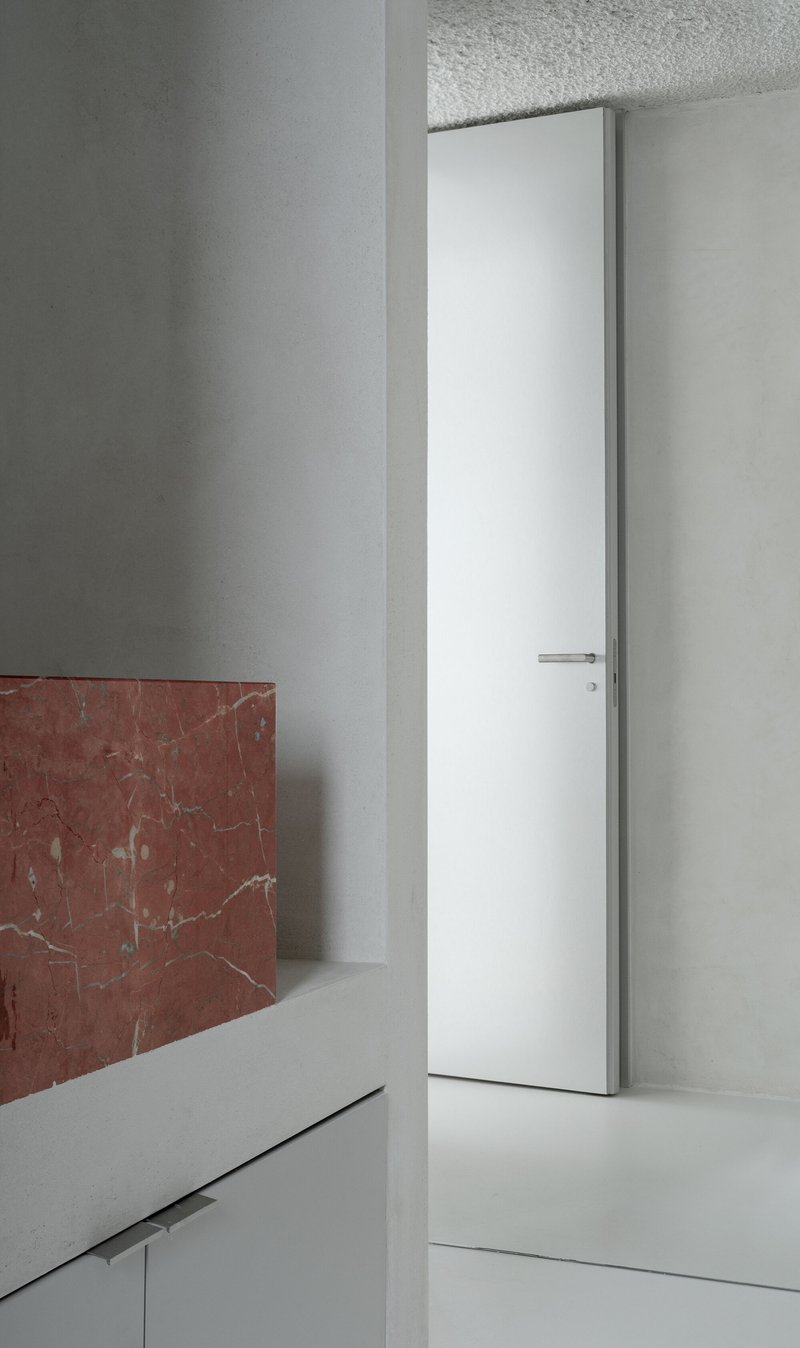 White flush door set into plaster walls with red marble wainscoting and terrazzo ceiling panel