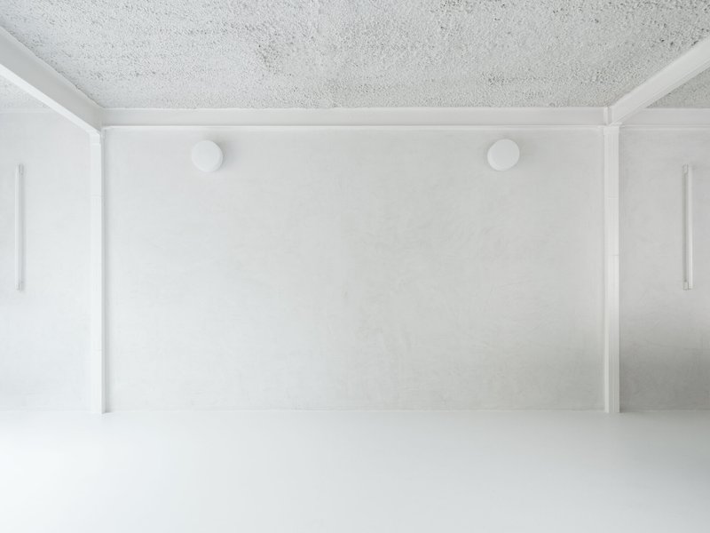 Wide interior room with white walls, terrazzo ceiling, white resin floor and two circular ceiling lights