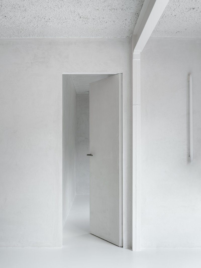 Open doorway framing a white corridor with terrazzo ceiling and continuous plaster walls