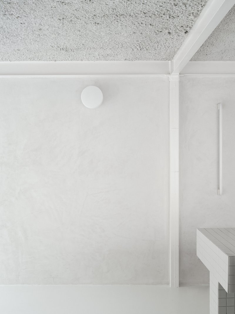 Top-down view of a white plaster ceiling with exposed concrete above and partial timber bench below