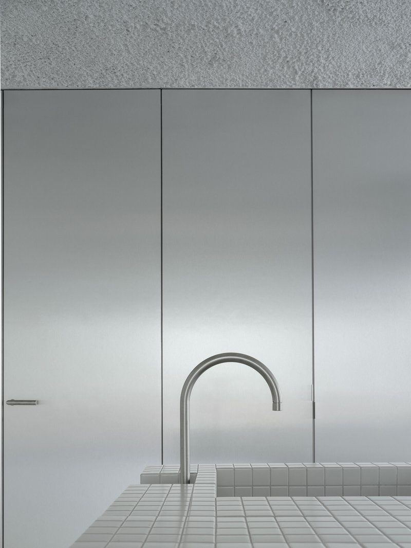 Close-up of a curved stainless steel faucet rising from a white mosaic tiled counter