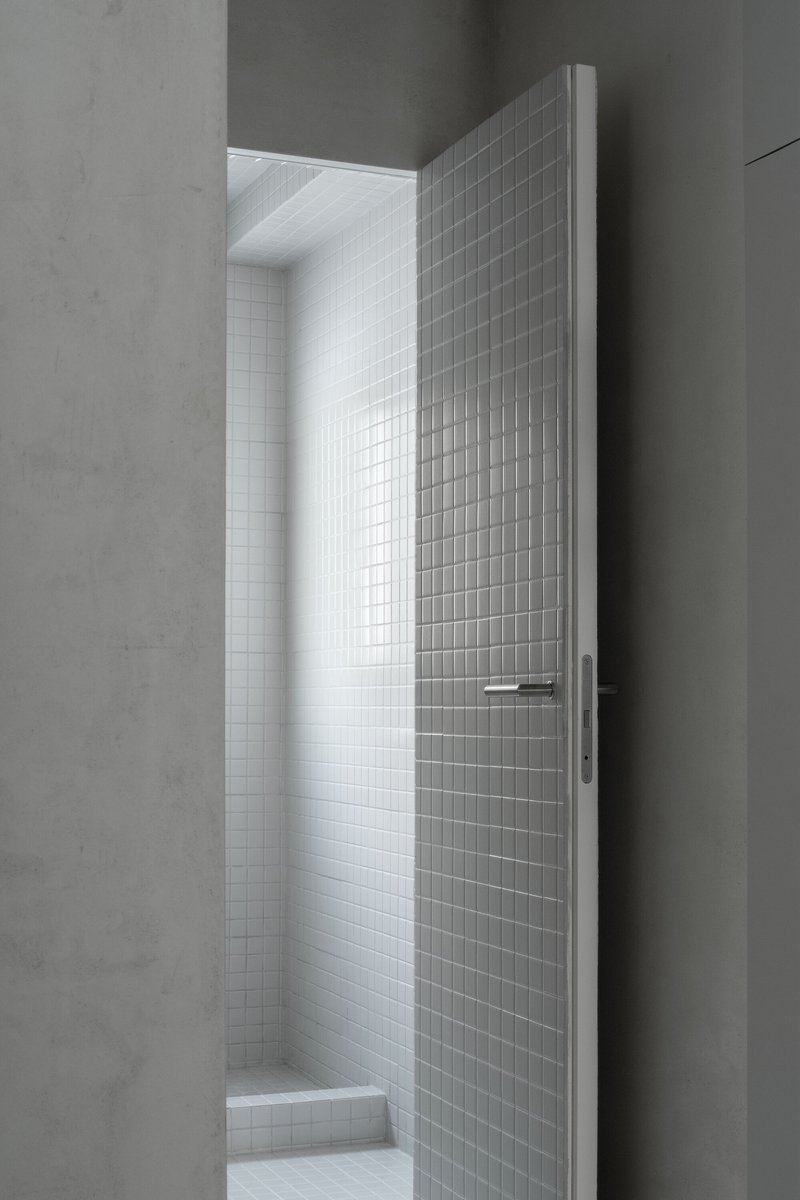 Narrow doorway opening to white mosaic tiled room lit by natural daylight from above