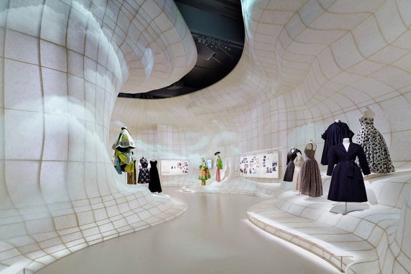 Organic white-tiled gallery walls with recessed alcoves displaying garments and collateral beneath gridded domes