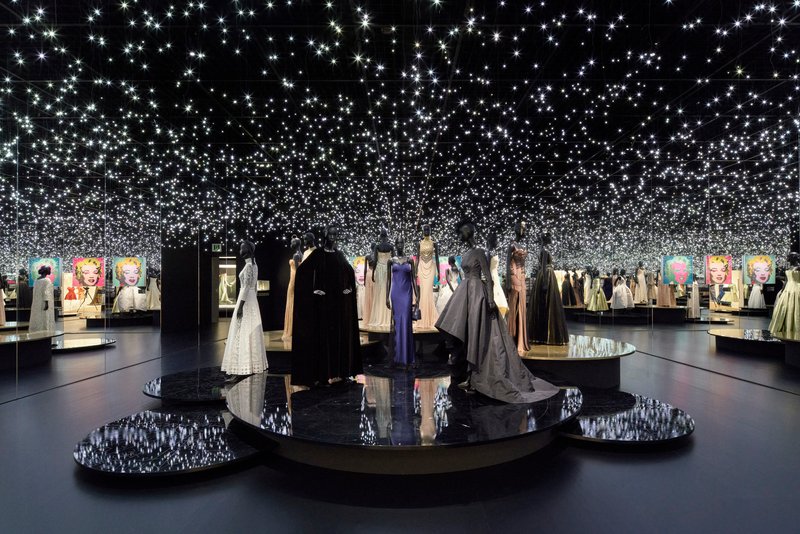 Black gallery space with circular platforms beneath a ceiling covered in thousands of small lights