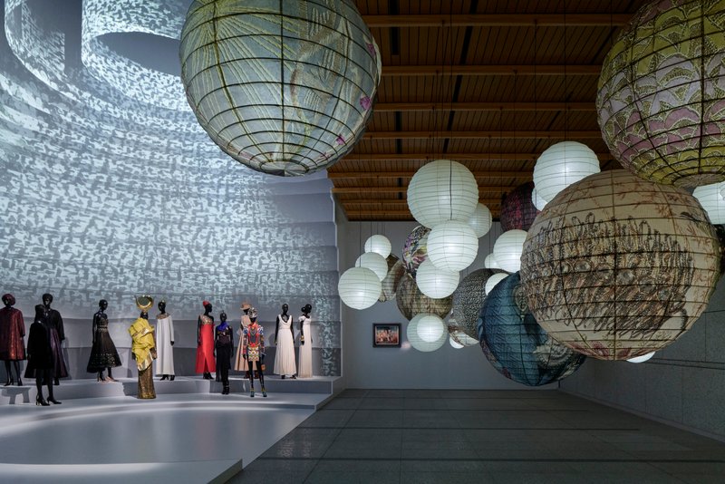 Large spherical paper lanterns hanging from a timber ceiling above a gallery with projected light patterns