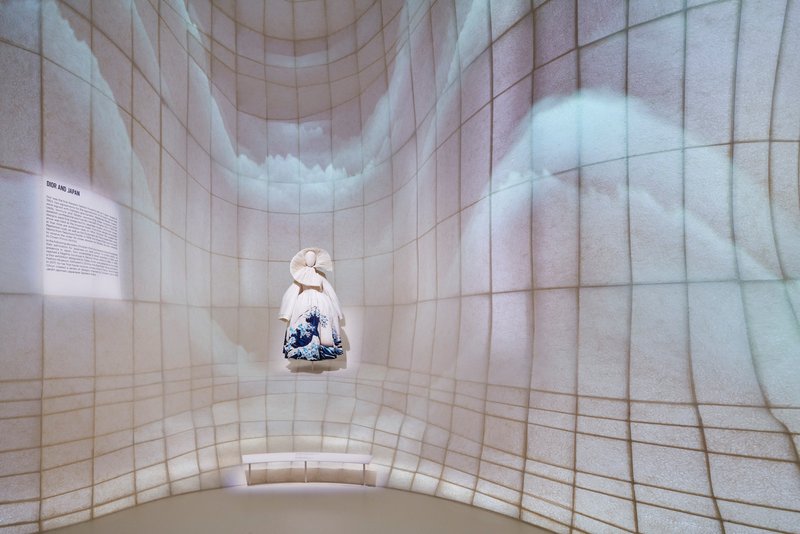 Single garment displayed in a curved alcove with projected imagery on the tiled walls
