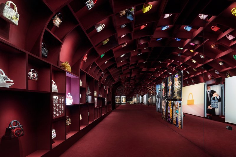Barrel-vaulted gallery with burgundy gridded shelving displaying handbags and illuminated niches