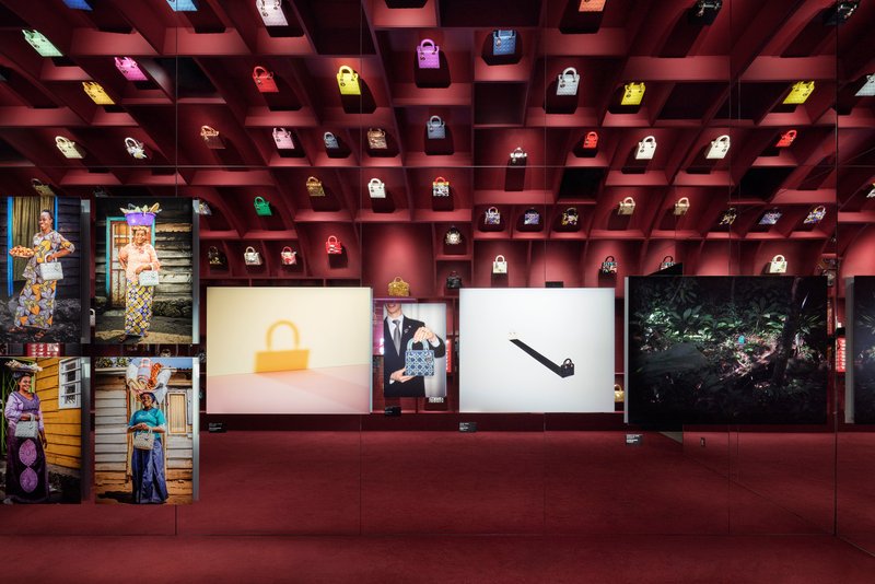 Coffered ceiling grid displaying illuminated handbags above burgundy walls and backlit panels